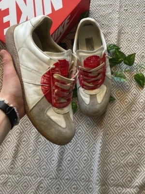 Vita sneakers med röd detalj - Unika vita sneakers från Nike med en stor röd cirkeldetalj på sidan och gråa partier vid tån. Skorna har klassisk snörning och en brun sula i gummi. Perfekta för dig som vill sticka ut med din stil.