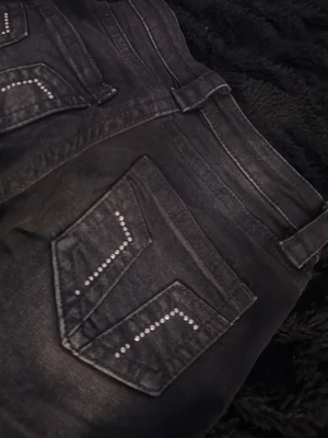 Svarta utsvängda jeans med nitar - Snygga svarta utsvängda jeans från Ginatricot med dekorativa nitar på bakfickorna. Jeansen har klassisk femficksmodell, låg midja och dragkedjegylf. Materialet är stretchigt denim som sitter tight och bekvämt.