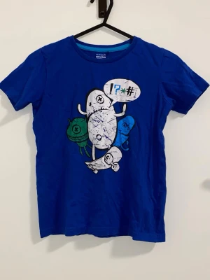 Blå t-shirt med tecknad print - Blå t-shirt med korta ärmar och ett färgglatt tecknat tryck framtill som föreställer figurer och pratbubbla. Rund halsringning och mjukt material som känns skönt mot huden. Perfekt för dig som gillar roliga och unika motiv.