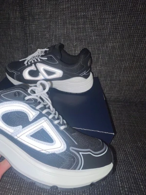 Svarta  sneakers med vit sula - Snygga svarta sneakers från  med vit och grå tjock sula. Skorna har vita snören och stora reflekterande detaljer med logga på sidan. Ovandelen är i mesh och syntetmaterial för en modern look. Perfekta för dig som vill sticka ut med exklusiva sneakers.