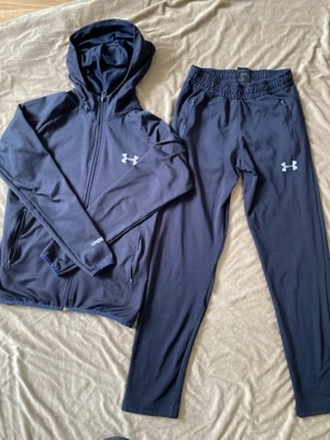  Under Armour tracksuit  - Snyggt marinblått tracksuit från Under Armour med zip-hoodie och matchande byxor. Setet har vita loggor på både jacka och byxor, dragkedjor på jackans fickor och elastisk midja på byxorna. Perfekt för allt✨