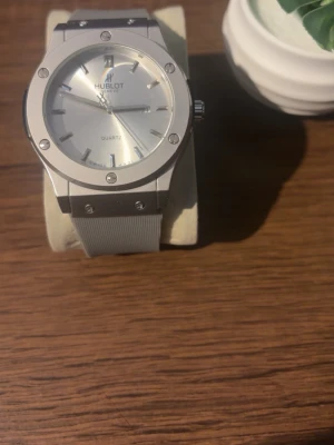 Klocka - Stilren klocka med silverfärgad urtavla och armband. Klockan har en rund form, markerade index och detaljer i metall. Perfekt accessoar för dig som gillar en clean och modern look.