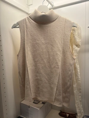 Beige ärmlös polotopp från Zara - Snygg beige ärmlös polotopp från Zara med ribbad hög krage. Toppen har en mjuk struktur och är perfekt för att styla lager på lager. Enkel och stilren design som passar till många olika looks.