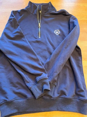 Mörkblå half-zip hoodie med logga - Snygg mörkblå hoodie från Morris med halv dragkedja och hög krage. Tillverkad i mjukt bomullsmaterial för skön känsla. Aldrig använd, tror det är storlek S men det står ej.