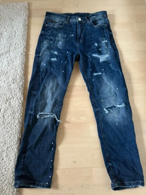 Mörkblå supply demand slitna jeans med hål, storlek L 12-13 år. L 12-13 år. - Säljer ett par mörkblå jeans med slitningar, hål vid knäna och stänkdetaljer framtill. Jeansen har rak passform och klassisk femficksdesign, använda 2 gånger bara.
