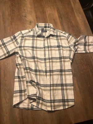 Rutig skjorta från Polo Ralph Lauren - Snygg rutig skjorta från Polo Ralph Lauren i beige, grått och vitt. Skjortan är tillverkad i 100% bomull och har klassisk krage och knäppning framtill. Perfekt för en avslappnad men stilren look.
