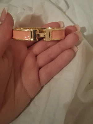  orange guldarmband - Snyggt armband i orange emalj med guldfärgade metalldetaljer och klassiskt spänne. Stilren och ikonisk design som lyfter vilken outfit som helst. Perfekt accessoar för dig som gillar lyxiga detaljer och trendiga smycken.