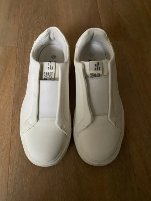 Vita slip-on sneakers från 157 - Stilrena vita slip-on sneakers från 157 med minimalistisk design. Skorna har elastiskt band över vristen istället för snörning och är tillverkade i ett slätt syntetmaterial med textilfoder. Perfekta för en clean och modern look. Kolla gärna mina andra annonser❗️