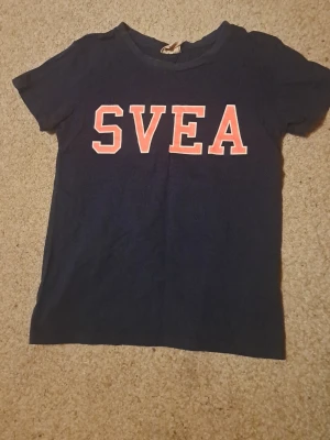 Mörkblå SVEA t-shirt med tryck - Snygg mörkblå t-shirt från SVEA med stort rosa och vitt tryck. Klassisk rund halsringning och korta ärmar. Perfekt för dig som gillar sportig och enkel stil. Tillverkad i mjuk bomull för skön känsla hela dagen. Ger en 2000s yoga style vibe som nu är trendig, samt en y2k style vibe. Kan användas för både sport men också till jeans. Inga defekter eller fläckar. Storlek 160/170 o jag beskriver det som XS/S