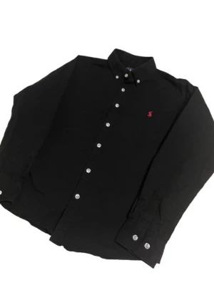 Svart skjorta från Ralph Lauren - Klassisk svart skjorta från Ralph Lauren med knappstängning och vit knappdetalj. Skjortan har lång ärm och en liten röd broderad logga på bröstet. Perfekt för en stilren look.