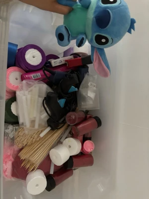 Stor pyssellåda med material och lim - En stor plastlåda fylld med pysselmaterial som färgat papper, glitter, limstavar, grillpinnar, limpistoler, färgade flaskor och en blå Stitch-mjukis. Perfekt för kreativa projekt och DIY-pyssel. Allt samlat i en praktisk förvaringslåda. Detta är perfekt till dig som vill börja göra satinblommor du får all tillbehör du behöver om ni exakt vill veta va ni får med i lådan får ni gärna höra av er 