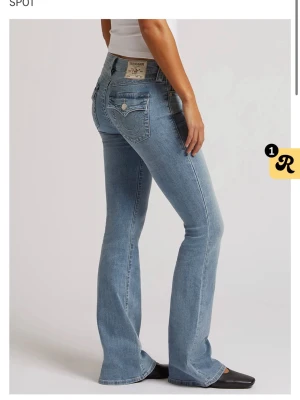 Blå bootcut jeans från True Religion - Säljer ett par ljusblå bootcut jeans från True Religion med klassiska fickdetaljer och logopatch bak. Jeansen har en snygg tvätt och markerade sömmar, samt stängs med knapp och dragkedja. Perfekta för en trendig och avslappnad look. Uppsydda av skräddare för att passa mig som är 160(orginal sömnad)