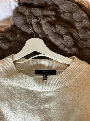 Beige stickad tröja från Vero Moda - Mysig beige stickad tröja från Vero Moda med rund halsringning och långa ärmar. Tröjan har en enkel, klassisk design med ribbade muddar vid hals, ärmslut och nederkant. Perfekt att matcha med jeans eller kjol för en avslappnad look.