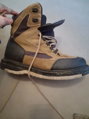 Bruna och svarta kängor med grov sula - Säljer ett par bruna och svarta kängor med högt skaft och grov, ljus sula. Kängorna har snörning och detaljer i både mocka och textil. Perfekta för dig som gillar en robust och cool stil.