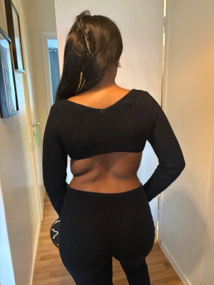 Svart ribbad jumpsuit med cut-outs - Säljer en svart, ribbad jumpsuit med långa ärmar och djupa cut-outs i sidorna. Framtill har den en snygg snörning över bröstet och en djup urringning. Materialet är stretchigt och följsamt, perfekt för dig som vill sticka ut. Ingen synlig logga eller märke.
