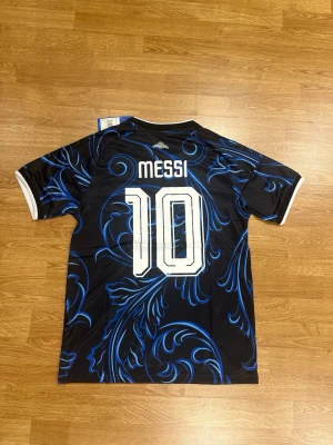 Argentina Messi tröja svart/blå Adidas - En av de mest hypeade VM tröjor, Argentinas bortaställ för VM 2026 med Lionel Messi 10 på ryggen finns i flera storlekar. Vid köp av 2 tröjor eller fler bjuder vi på frakt. Helt ny!!!