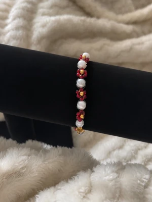 Pärlarmband med röda blommor - Ett armband med vita pärlor och små röda blommor av pärlor. 