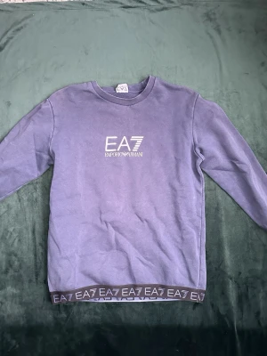 Blå EA7 Emporio Armani sweatshirt - Snygg blå sweatshirt från EA7 Emporio Armani med tryckt logga på bröstet och elastisk kant med EA7-tryck nedtill. Tröjan har rund halsringning och långa ärmar. Perfekt för en trendig och avslappnad stil. Pris kan diskuteras. MVH stentorparchive⚓️