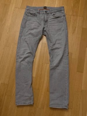 Grå jeans från BOSS - Snygga grå jeans från BOSS med klassisk femficksdesign och raka ben. Jeansen har diskreta sömmar och en liten BOSS-logga på myntfickan. Perfekta för en stilren och avslappnad look.