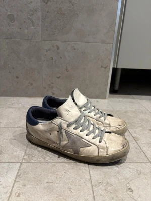 Golden Goose vita sneakers med grå stjärna - Snygga vita sneakers från Golden Goose med grå stjärna på sidan, 7/10 i skick otvättade men kan bli riktigt fräscha priset ej hugget i sten do jag är behov av pengar🤗👍storlek 41-42 dom är även äkta!👍