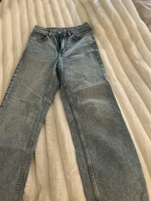 Ljusblå raka jeans i klassisk modell - Säljer ett par ljusblå jeans med rak passform och hög midja. Jeansen har fem fickor, bälteshällor och stängs med knapp och dragkedja. Tillverkade i klassisk denim med en vintagekänsla. Perfekta för en avslappnad och trendig look.