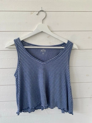 Blåvit randig linnetopp Hollister - Säljer en blå och vit randig linnetopp från Hollister. Toppen har v-ringning, är ärmlös och har en lös passform med vågig kant nertill. Perfekt för varma dagar och enkel att matcha med jeans eller shorts.