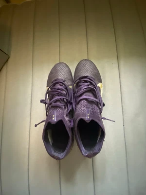 Nike Mercurial ZM Vapor 16 Elite KM FG - Säljer ett par lila Nike Mercurial fotbollsskor med guldiga detaljer och snörning. Skorna har en strumpliknande passform och är tillverkade i syntetmaterial för bästa grepp och känsla på planen. Perfekta för dig som vill sticka ut på fotbollsplanen.