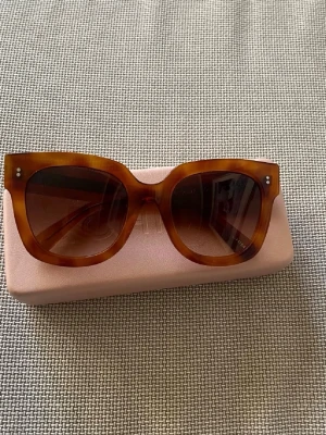 Bruna solglasögon i light tortoise - Snygga solglasögon i light tortoise med bred båge och fyrkantig form. Färgen är brunmelerad och glasen är mörka. Perfekt accessoar för att lyfta din stil. Kommer med ett rosa fodral.