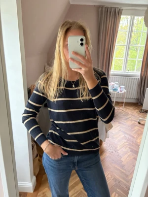 Svart- och beige randig tröja - Snygg långärmad tröja med svarta och beigea horisontella ränder. Tröjan har rund halsringning och är i ett mjukt, stickat material. Perfekt för en avslappnad och stilren look.