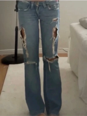 Ljusblå slitna bootcut jeans från true religion - Säljer ett par ljusblå bootcut jeans med stora slitningar och hål på båda benen. Jeansen har låg midja, ifrån true religion!