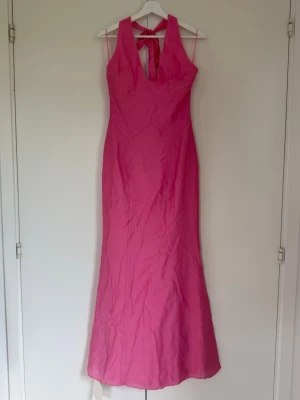 Rosa långklänning från Adoore - Snygg långklänning i rosa färg från Adoore. Klänningen har halterneck med knyt i nacken och en figurnära passform som ger en elegant siluett. Perfekt för dig som vill sticka ut med en färgstark look💕💕 Hekt ny och aldrig använd!