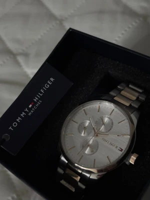 Tommy Hilfiger silverfärgad klocka - Stilren klocka från Tommy Hilfiger med silverfärgad urtavla och länkarmband i både silver och guldton. Klockan har tre mindre urtavlor och klassisk design med diskreta detaljer. Perfekt accessoar för att lyfta din outfit.