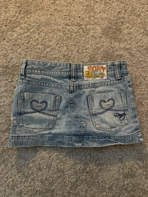 Ljusblå jeanskjol från Roxy - Säljer denna jätte söta jeanstjolen med hjärtan på fickorna! Den är för liten på mig och storleken säger ”10” men skulle säga att den passar som en XXS-XS. Obssss, vänstra fickan har gått lite sönder 