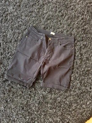 Svarta jeansshorts med fem fickor - Svarta jeansshorts med klassisk femficksdesign och gylf med knapp. Shorts i rak modell med bälteshällor och bakfickor. Perfekta för en avslappnad stil under varmare dagar.