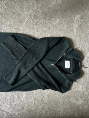 Mörkgrön stickad tröja Jack & Jones  - Mörkgrön stickad tröja från Jack & Jones med halv dragkedja och hög krage. Tröjan har ribbstickad struktur och långa ärmar, perfekt för lager-på-lager och en chill look. Storlek S men passar även M
