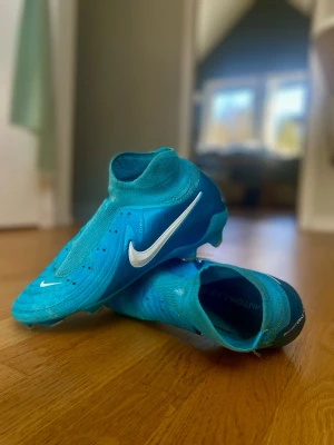 Nike Phantom Luna PRO - Jag säljer ett par fotbollsskor som jag köpte för ett år sedan, men blev skadad direkt efter och nu är de för små för mig. De har knappast använts. Modellen på skorna är PRO, så nypris 1299kr. Pris kan diskuteras, jag ändrar gärna på priset om du vill. Tyvärr så tog jag ut mina skosnören, och har bara ett skosnöre som tillhör, men om du vill så kan jag köpa det snöra som saknas innan jag skickar det till er utan att det påverkar priset! Skorna är i en fin himmelsblå färg⚽️👟🫐💙