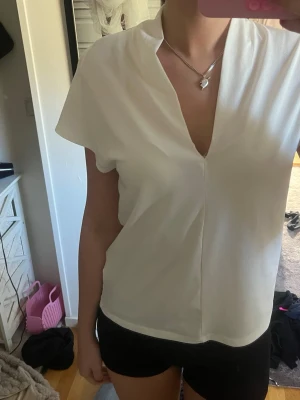 Vit v-ringad blus med kort ärm - Stilren vit blus med djup v-ringning och korta ärmar. Blusen har en rak passform och är tillverkad i ett lätt, slätt tyg som ger en fräsch och modern look. Perfekt att matcha med både jeans och kjol för en clean stil.