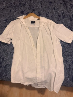 Vit linneskjorta från Only & Sons - Säljer en vit kortärmad skjorta från Only & Sons i linnematerial. Skjortan har klassisk krage, knappar framtill och en slim passform. Perfekt för varma dagar och enkel att styla till olika outfits.