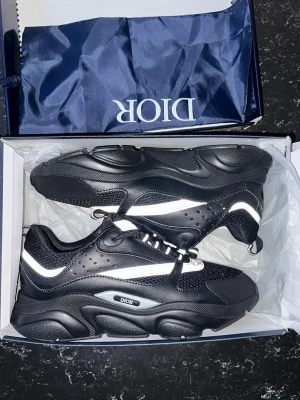B22 sneakers - Snygga svarta  sneakers med vita detaljer och reflekterande inslag. Skorna har chunky sula, meshpaneler och perforerade partier för extra stil. Märket syns tydligt på sidan. Perfekta för dig som vill sticka ut med exklusiva sneakers.