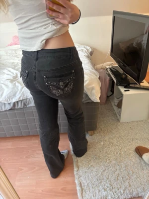 Svarta bootcut jeans med nitar - Säljer ett par svarta bootcut jeans med snygga nitar på fickorna fram och bak. Jeansen har låg midja och dekorativa detaljer på bakfickorna. Perfekta för dig som gillar en edgy stil.