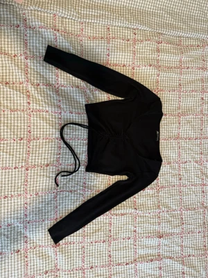 Svart croppad topp med snörning - Svart långärmad croppad topp från NA-KD med snygg snörning framtill. Toppen är ribbad och har en tight passform som framhäver figuren. 