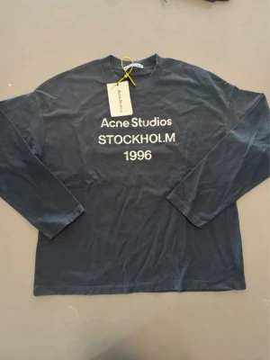 Acne Studios longsleeve - Snygg svart longsleeve från Acne Studios med vit text 'Acne Studios STOCKHOLM 1996' på bröstet. Klassisk passform och rund halsringning. Perfekt för en stilren och avslappnad look. Aldrig använd| skick: 10/10|