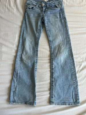 Ljusblå bootcut jeans - Säljer ett par ljusblå bootcut jeans med klassisk femficksdesign och utsvängda ben. Jeansen har normalhög midja och är tillverkade i denim med lätt tvättad look. Perfekta för en avslappnad och trendig stil.