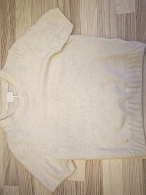 Vit stickad kortärmad topp H&M - Mysig vit stickad topp från H&M med korta ärmar och rund hals. Perfekt för lager-på-lager och enkel att matcha med olika outfits. Ribbstickade detaljer vid ärmslut, hals och nederkant ger en snygg finish.