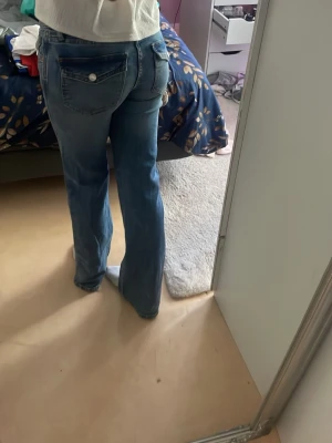 Blå bootcut jeans med fickdetaljer - Snygga blå flared jeans med klassiska fickor bak och fram, samt silverfärgade knappar på bakfickorna. Jeansen har en lätt tvättad look och normal midja. Perfekta för dig som gillar en avslappnad men trendig stil. Jeansen är från lager 157 och är perfekt längd på mig som är 170cm. Liknar true religion jeansen
