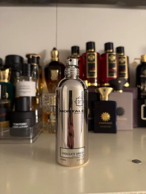Montale Chocolate Greedy parfym 100ml - Montale Chocolate Greedy är en lyxig parfym i en spegelblank, silverfärgad metallflaska med svart text och logga. Flaskan rymmer 100 ml och har en modern, stilren design som sticker ut i parfymhyllan. Perfekt för dig som gillar gourmanddofter.