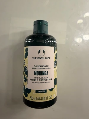 The Body Shop Moringa Conditioner - Balsam från The Body Shop med moringa, ger glans och skydd. Flaskan är grön med blommigt mönster och rymmer 250 ml. Passar dig som vill boosta hårets lyster och vårda det med veganska ingredienser.