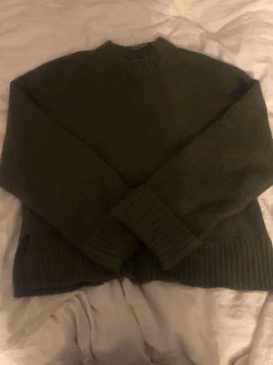 Mörkgrön stickad tröja - Mysig mörkgrön stickad tröja med rund halsringning och breda ribbstickade muddar vid ärmslut och nederkant. Perfekt för lager-på-lager och enkel att matcha med jeans eller kjol.