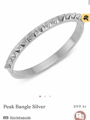 Silvrigt armband med nitar från Edblad - Snyggt och edgy armband i silverfärgad metall från Edblad. Armbandet har en oval form och är dekorerat med små spetsiga nitar runt hela. Perfekt accessoar för att ge din outfit en cool touch. Har haft den ett tag men aldrig använt.