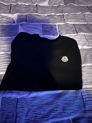 Svart Moncler t-shirt i bomull - Snygg svart t-shirt från Moncler med klassisk rund hals och Moncler-logga på bröstet. Tillverkad i 100% bomull för en skön och mjuk känsla. Perfekt till jeans eller shorts för en clean och stilren look.